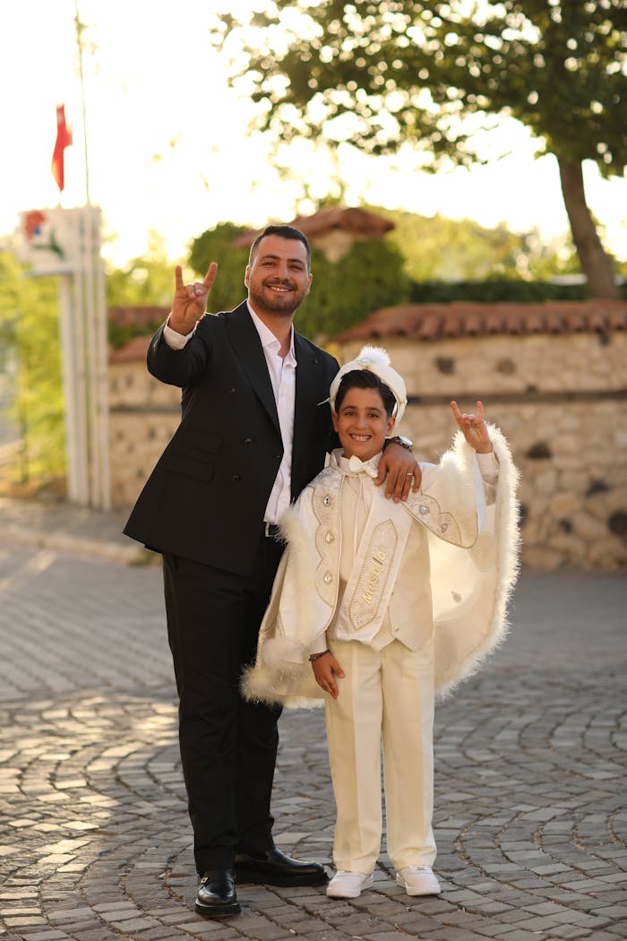 A father and son pose happily outdoors in elegant traditional clothes, signifying celebration.