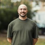 Portrait of a smiling man standing outdoors in a city park. Urban background with soft natural light.