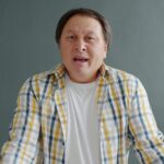A man in plaid shirt expressing surprise against a gray background.